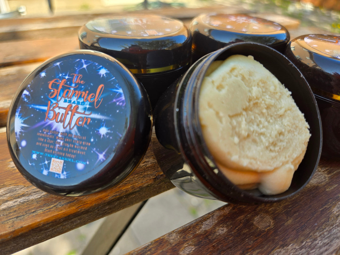 Starriel Beard Butter in black jars on a wooden table, with one jar open to show the creamy texture.